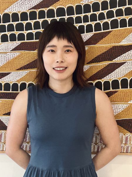 Person with shoulder length brown hair standing in front of artwork