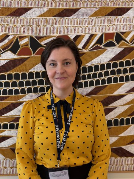 A person wearing a yellow shirt with short brown hair standing in front of artwork